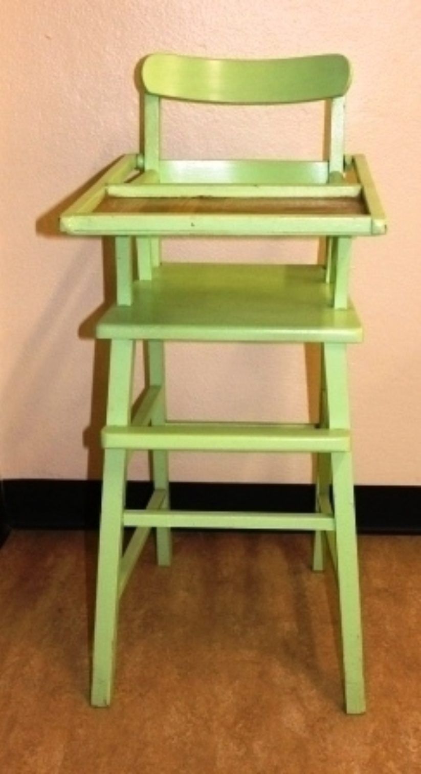 Light green high chair with tray on a wooden floor against a beige wall
