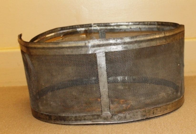 Small round metal mesh basket with a wire handle on a beige floor