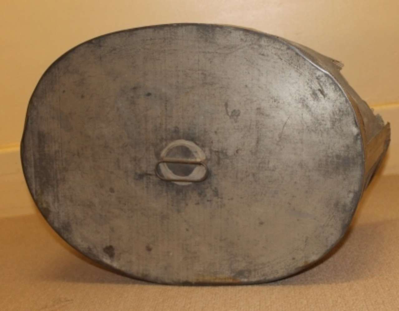 Oval gray metal lid with a central handle, shown against a tan background