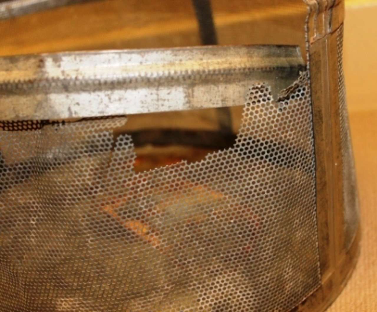Close-up of a metal mesh basket with rust and a wooden handle on a table