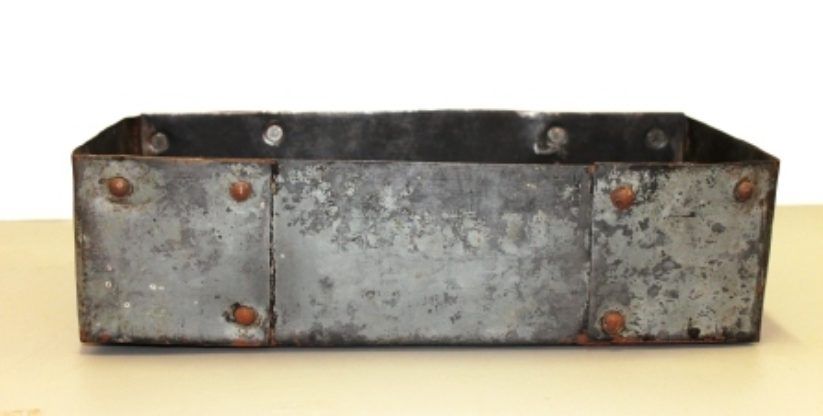 Weathered metal rectangular tray with rusty sides and bolt holes on a light surface