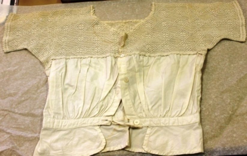 Vintage cream-colored lace and white fabric garment laid flat on a beige background