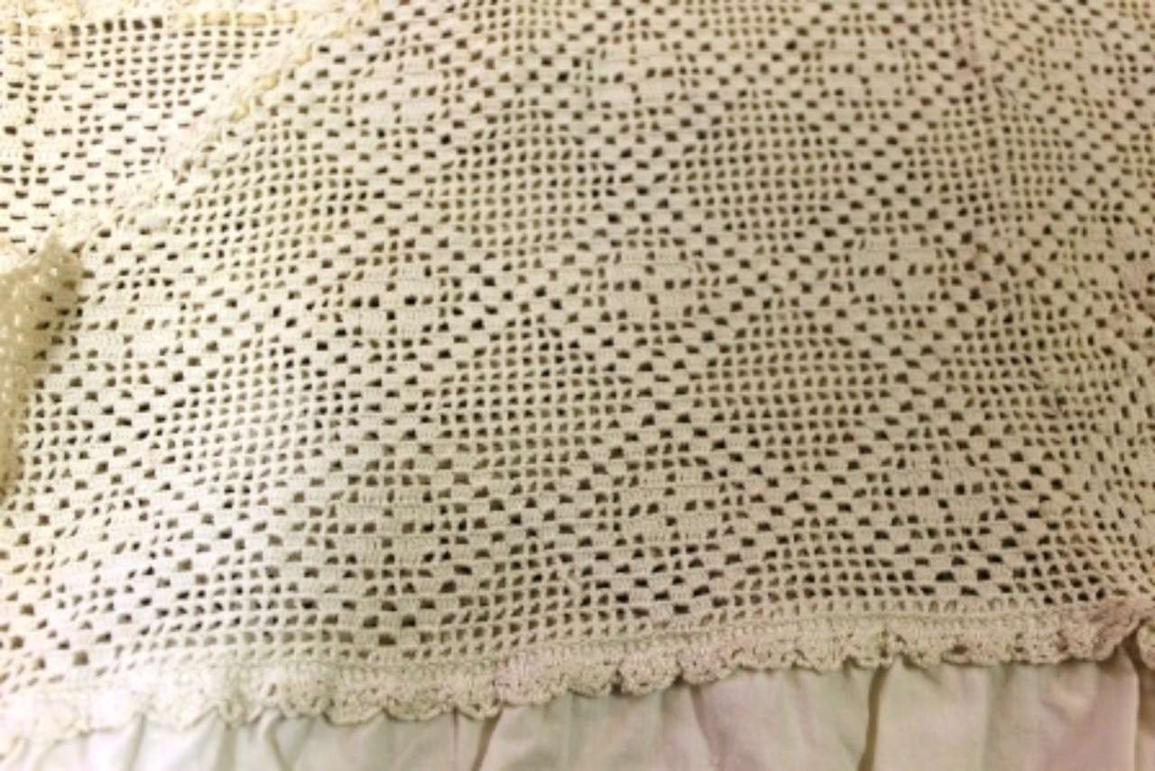 Close-up of a cream crochet fabric with a scalloped edge and ruffled hem