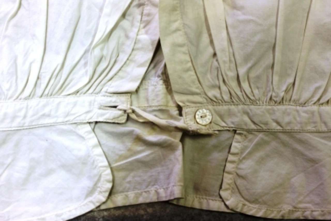 Close-up of a wrinkled beige jacket with a buttoned flap and gathered fabric details.