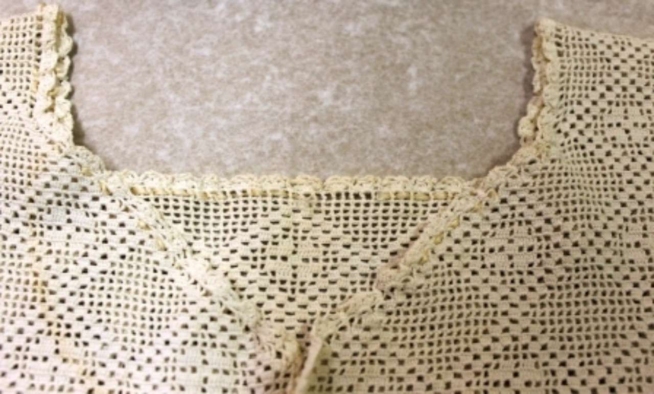 Cream crochet lace top with a scalloped neckline and openwork pattern laid flat on a beige surface
