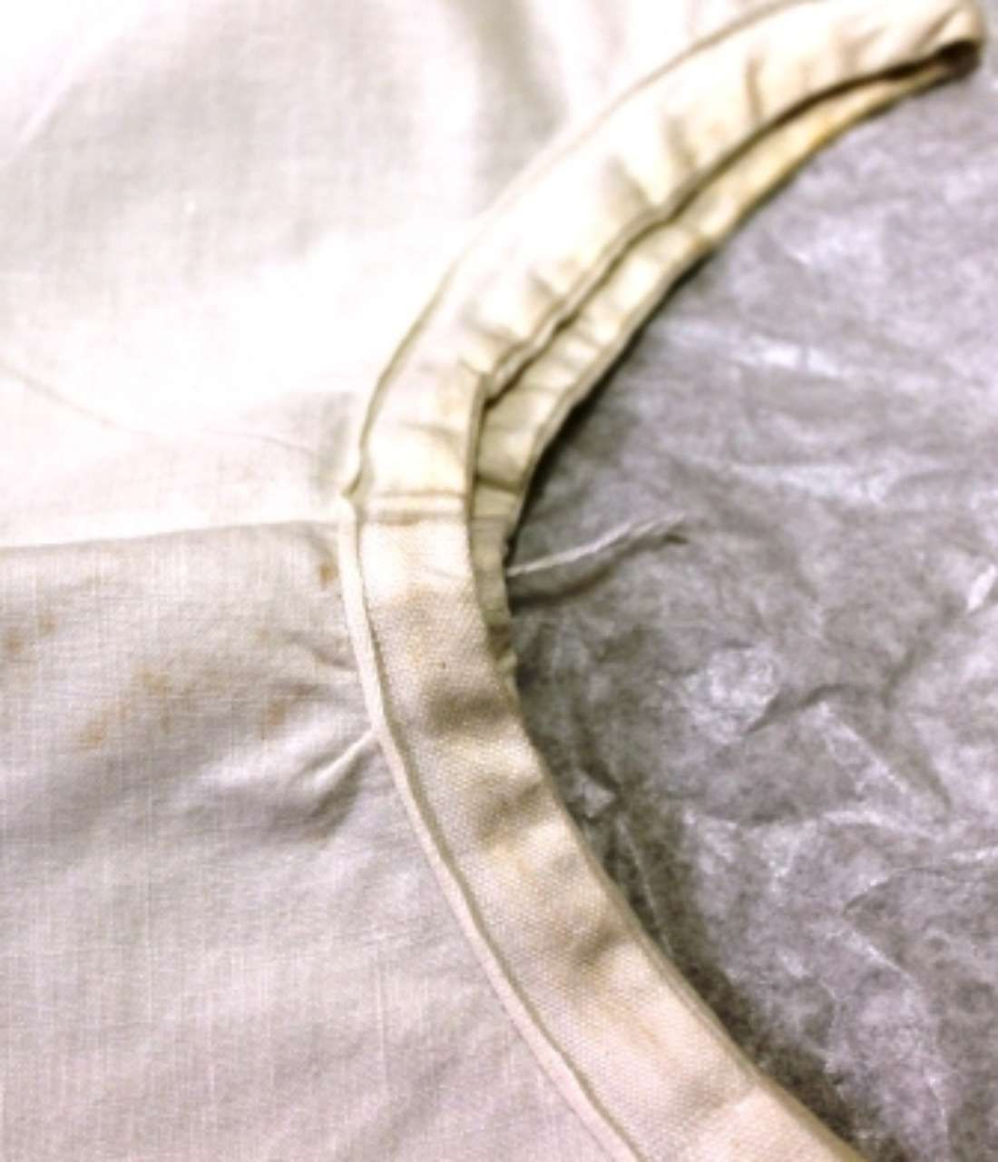 Close-up of a white fabric edge with stitching beside a crinkled gray liner