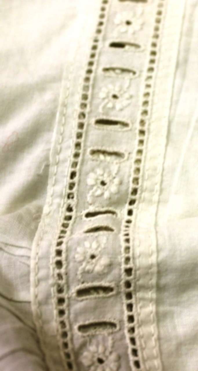 Close-up of white fabric with a vertical decorative stitched trim and button-like embroidered details