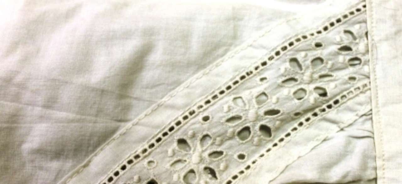 Close-up of white eyelet lace fabric with floral cutout embroidery and stitched trim