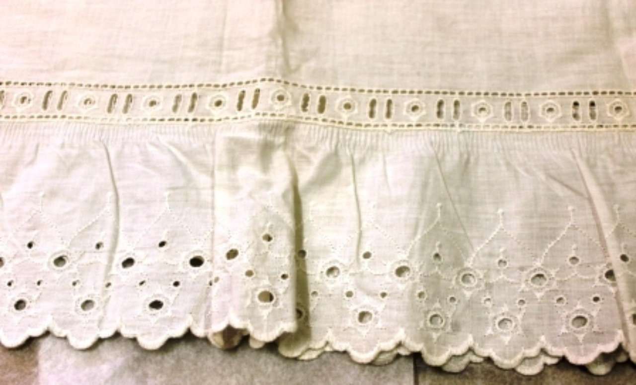 White embroidered lace fabric trim with scalloped edges and small cutout details on a white cloth background