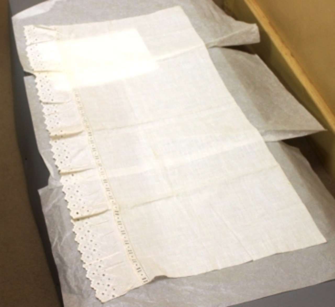 White lace-trimmed cloth folded on a box lid in a tan-walled room