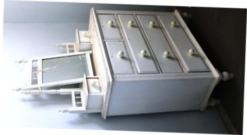 White wooden dresser with mirror and drawers, tilted on its side against a dark wall.