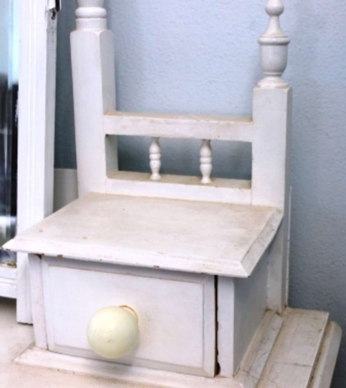 White wooden dollhouse with a slanted roof and small round knob, against a blue wall.