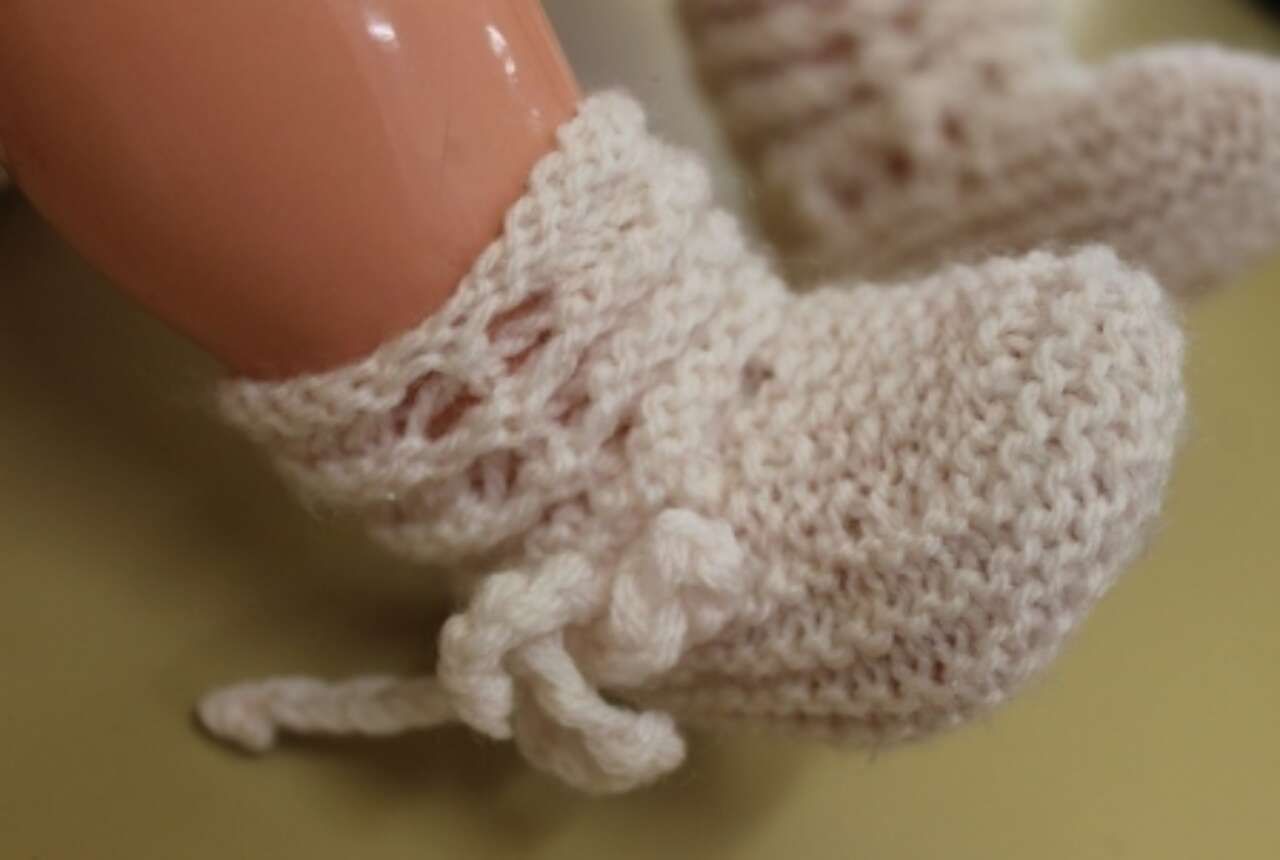 Close-up of a knitted beige bootie on a mannequin foot, tied with a small lace bow.