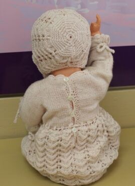 White crocheted doll seen from behind, sitting and pointing upward in a light dress against a soft background