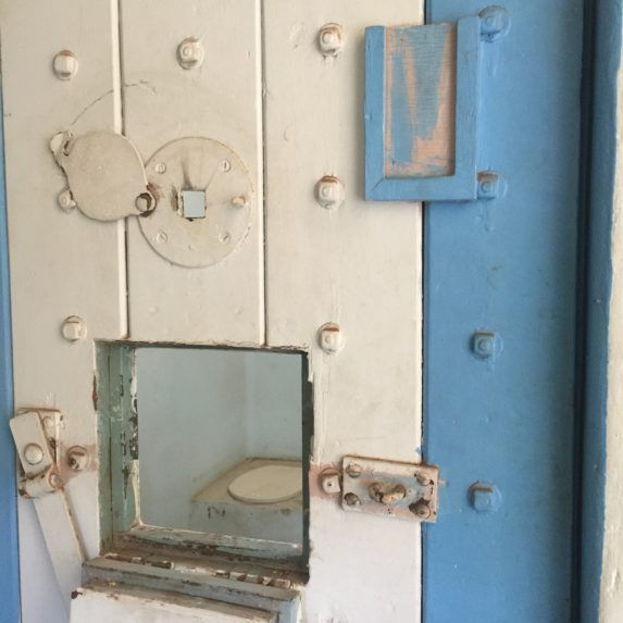 Blue and white metal door with bolts and a small glass opening, slightly ajar