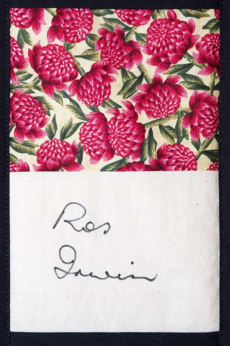 Raspberry floral fabric swatch with a handwritten signature on white paper below