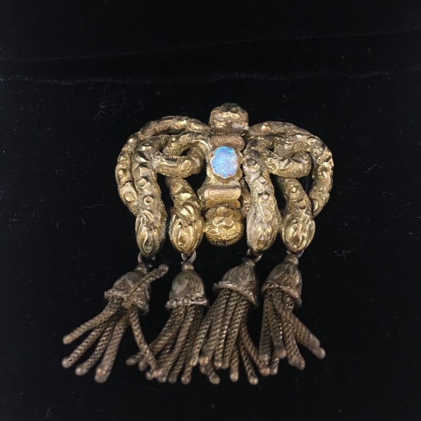 Gold ornate brooch with blue gem and dangling tassels on a black background