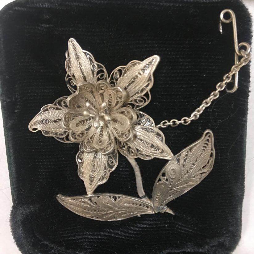 Silver filigree flower brooch with a leaf on a black velvet background