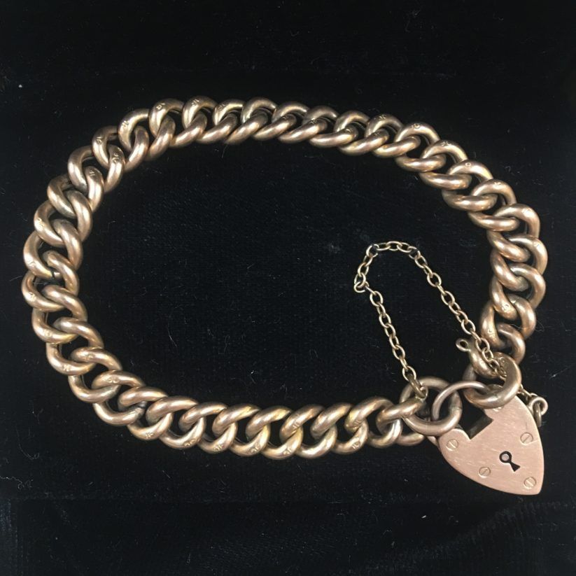 Silver chain bracelet with a heart-shaped lock and safety chain on a black background