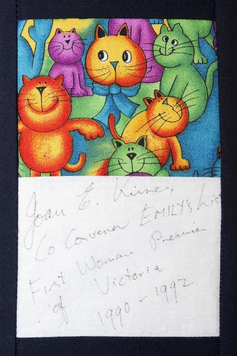 Colorful cartoon cats on blue fabric above a white note with faint pencil handwriting