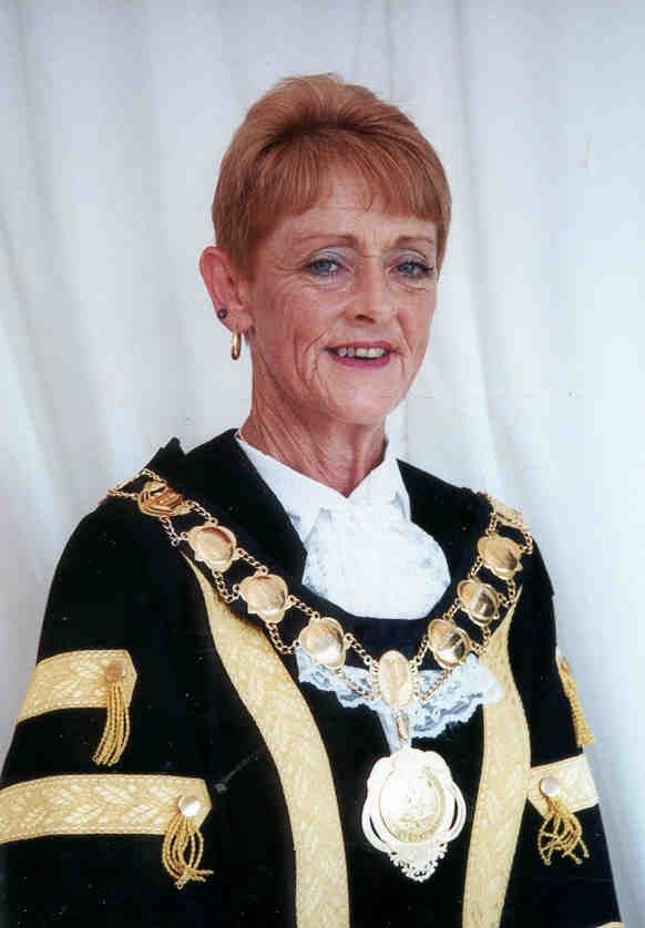 Woman in formal black-and-gold regalia with ceremonial chain, standing against a white backdrop