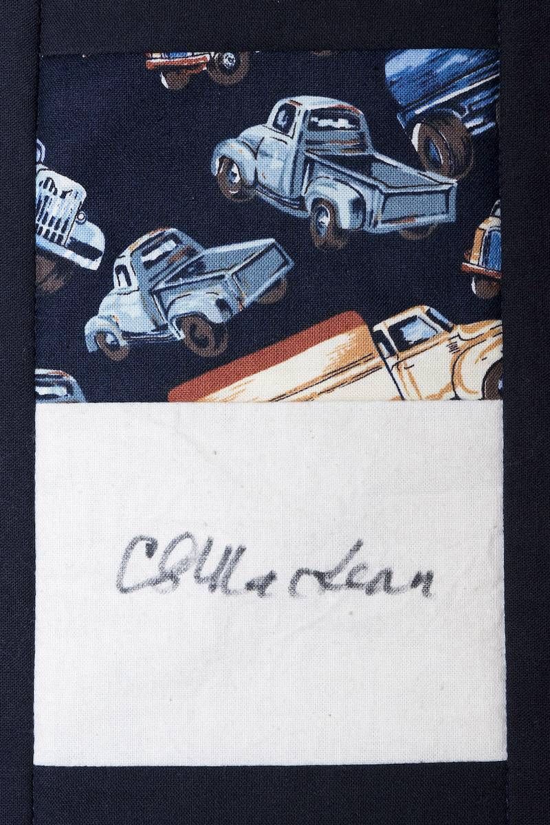 Handwritten word on white paper beneath a dark fabric with small truck prints