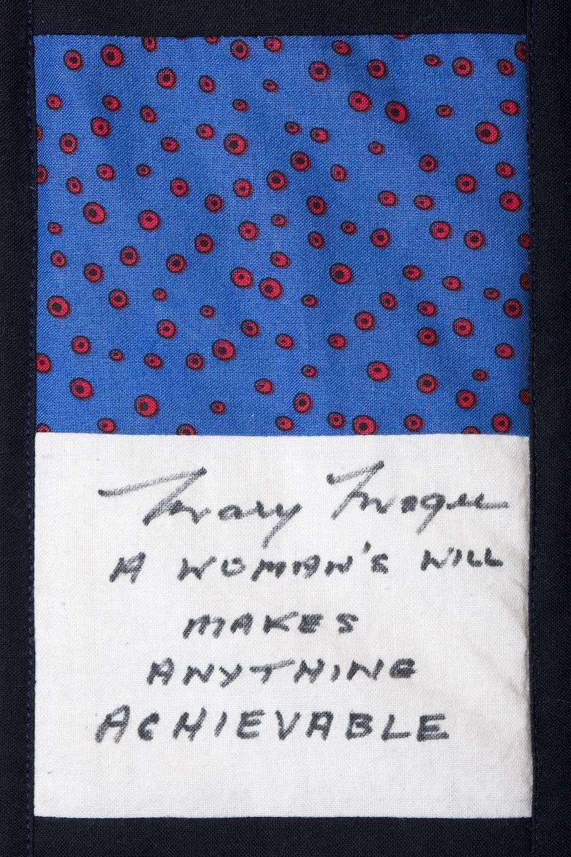 Handwritten note on white paper over blue patterned fabric: “Any woman’s nil makes anything achievable.”