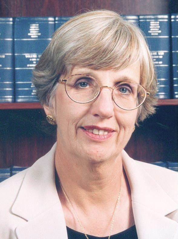 Portrait of a woman in glasses and a light blazer, standing before a bookshelf background