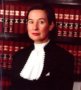 Portrait of a person in a black suit with a white necktie, standing before shelves of red law books