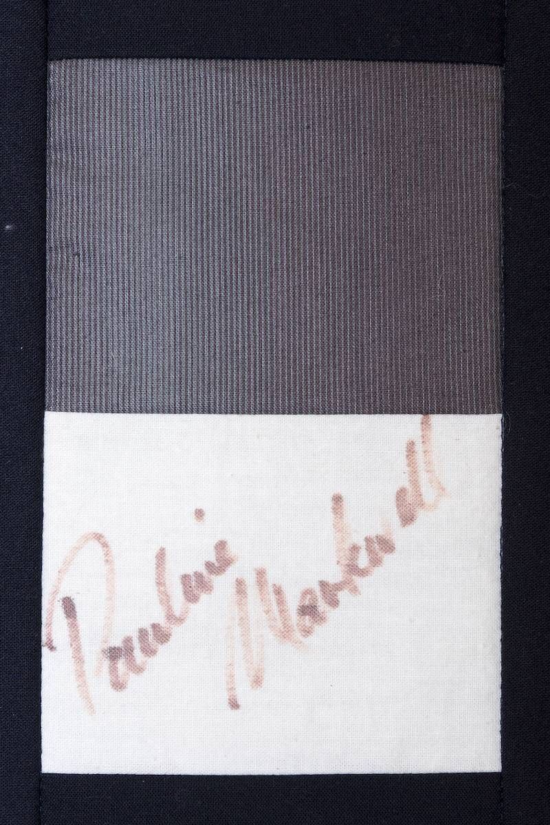 Dark gray textured fabric with a white band and faded pink handwritten text at the bottom.