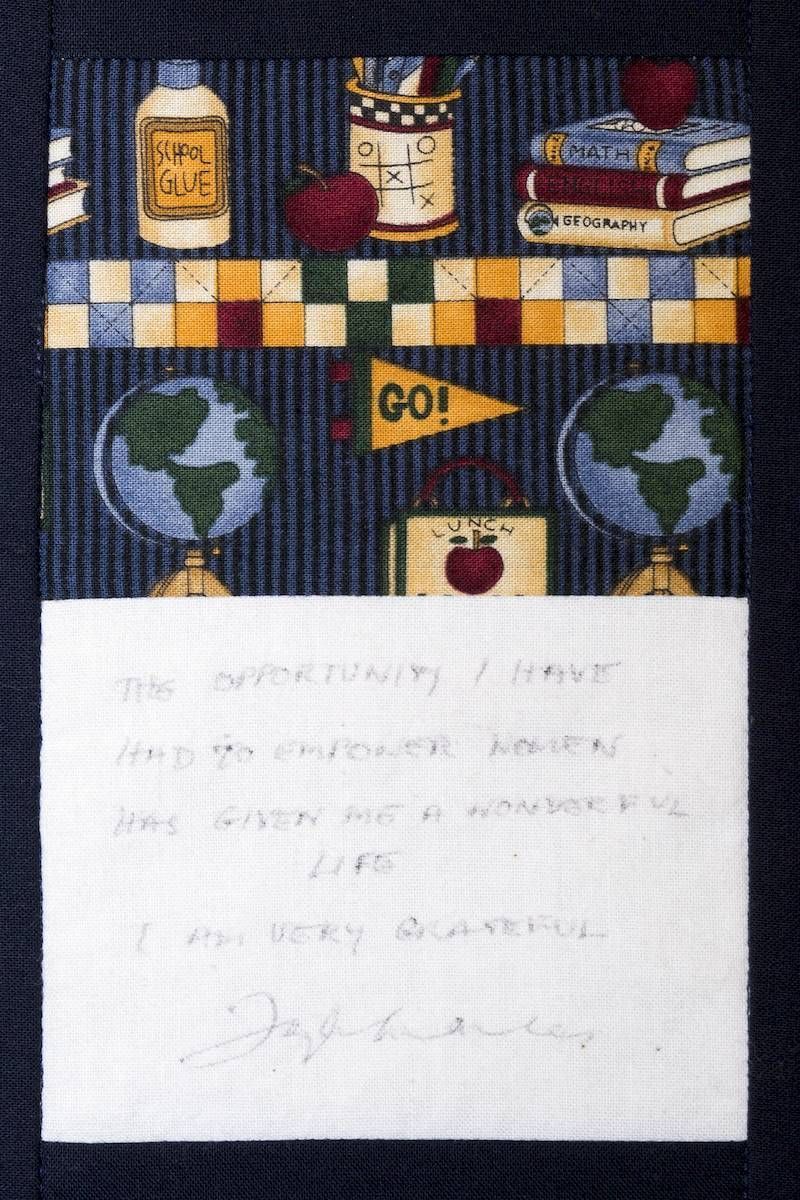 Handmade school-themed quilt with apples, globe, books, “GO!” flag, and a white handwritten note at the bottom