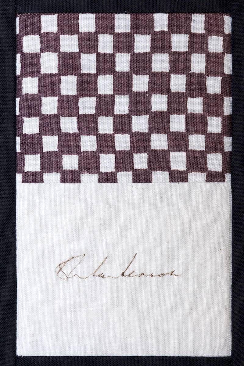 White card with a brown-and-white checkerboard band at top and a faint handwritten signature below.
