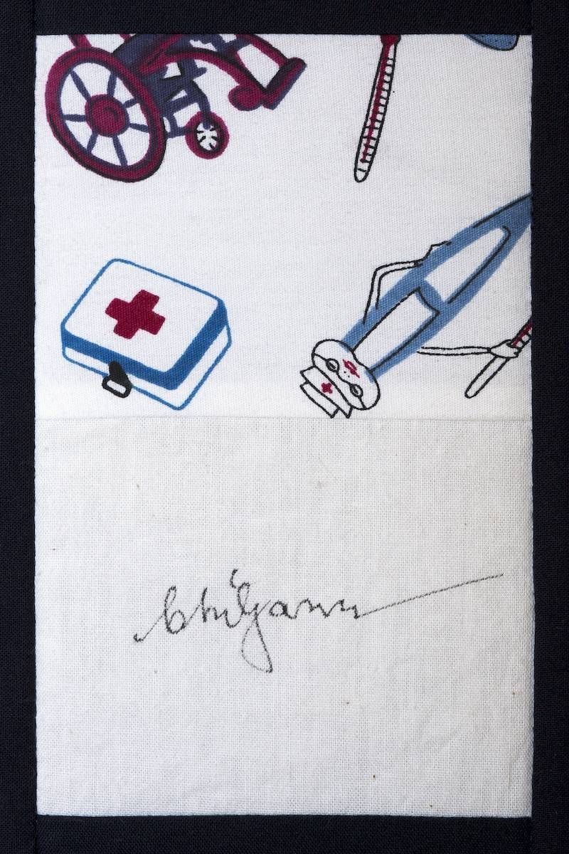 White cloth with small medical-themed prints: red wheelchair, blue first-aid kit, blue crutches, and a cursive signature.