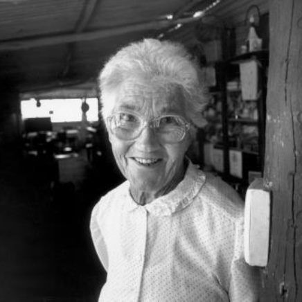 Smiling woman with glasses standing in a rustic indoor shop doorway