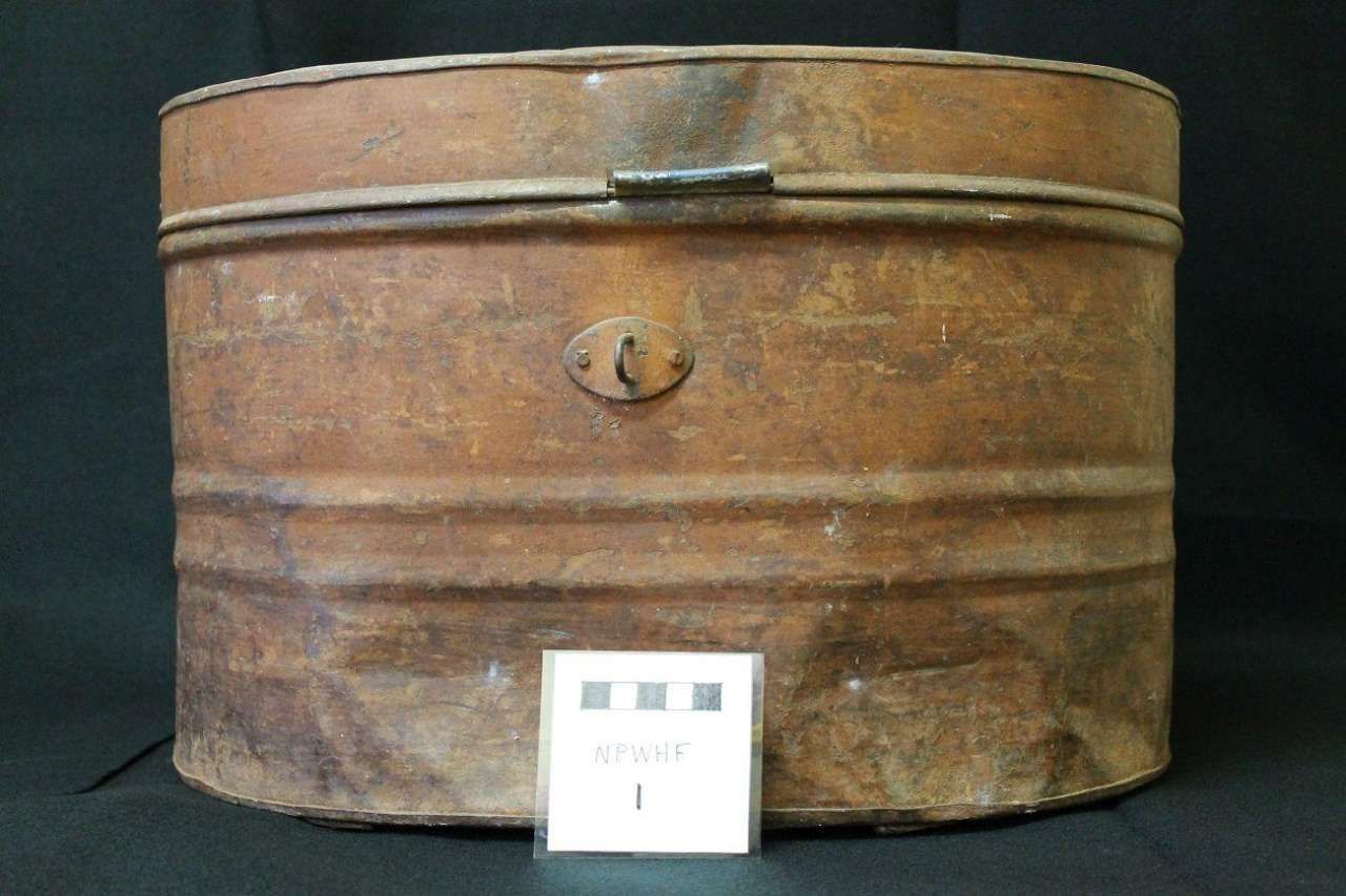 Rusty brown metal storage box with a latch, shown against a dark background