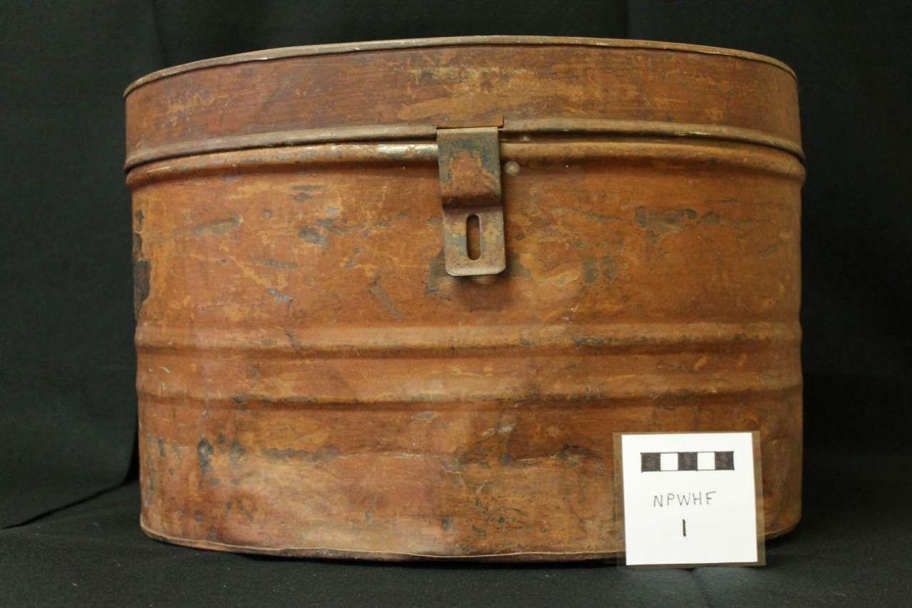 Rusty brown metal trunk with a latch, shown against a dark background