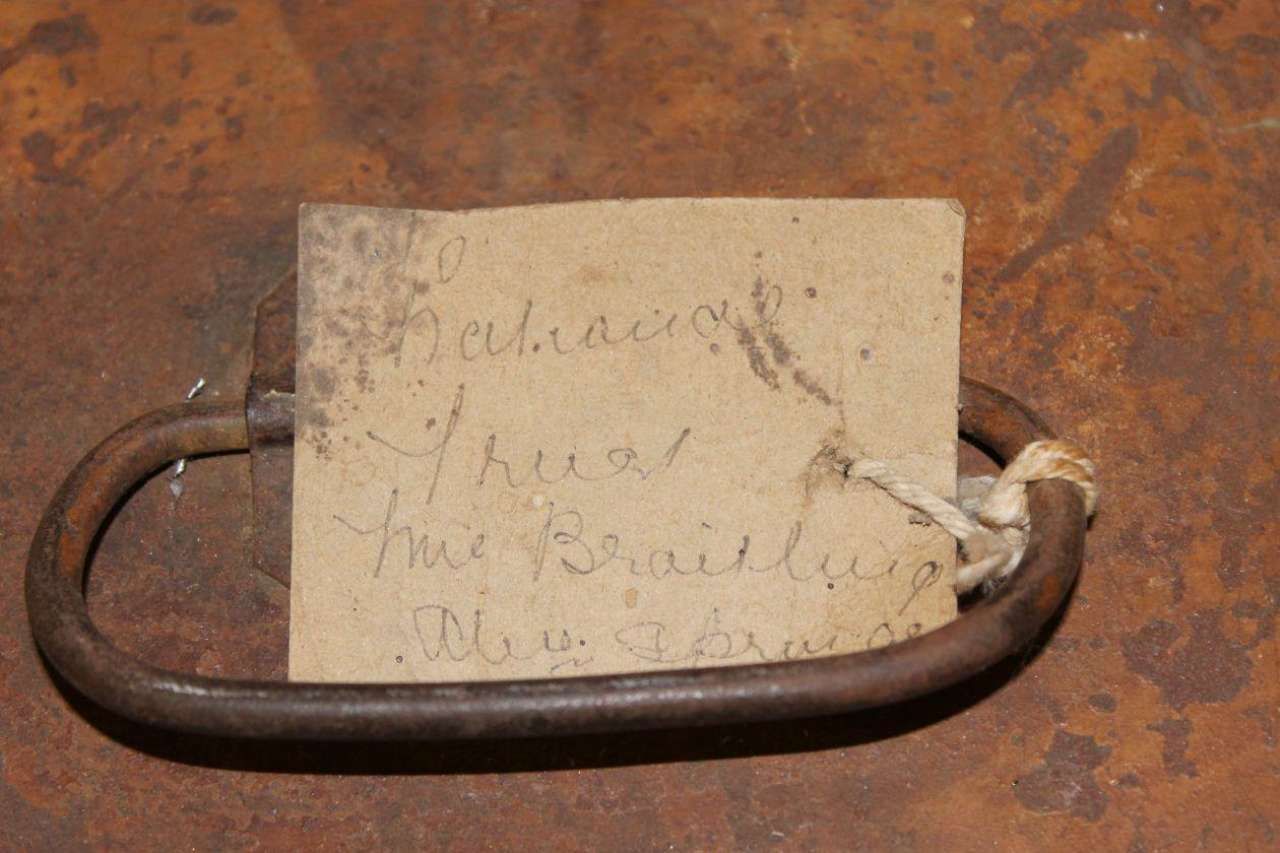 Rusty metal shackle with a handwritten paper tag attached by string