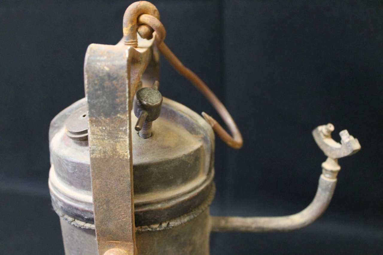 Rusty metal canister lid with attached clamp and curved tubing on a dark background