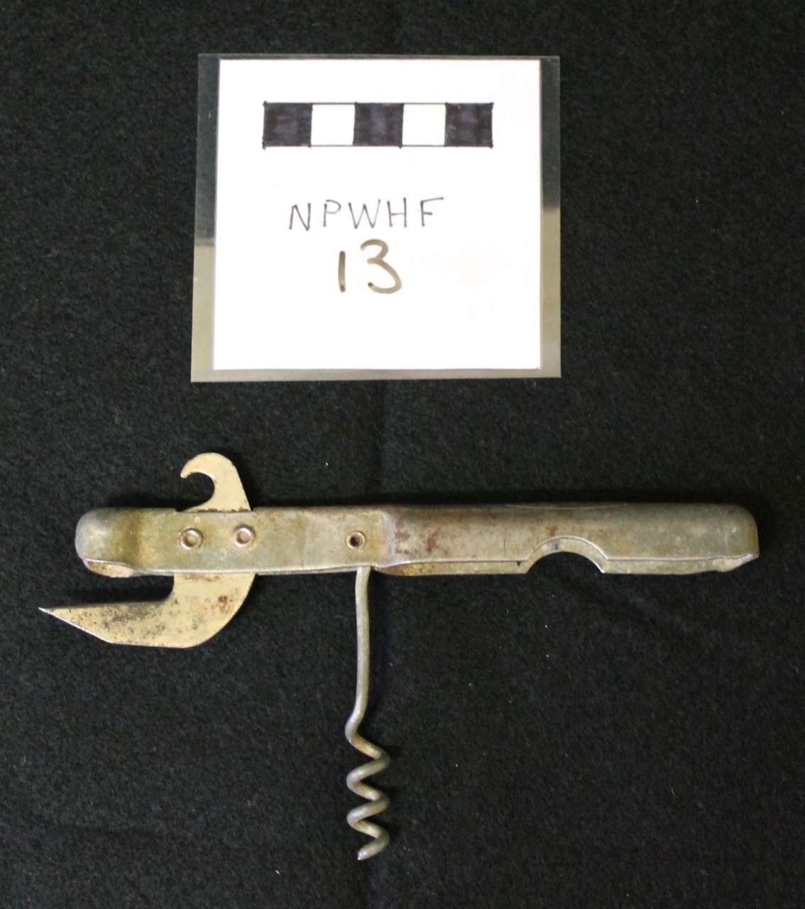 Old metal corkscrew below a labeled museum tag on a dark background