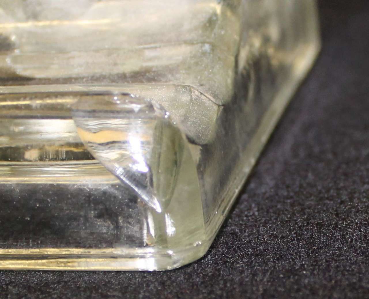 Close-up of a clear glass bottle corner on a dark fabric surface