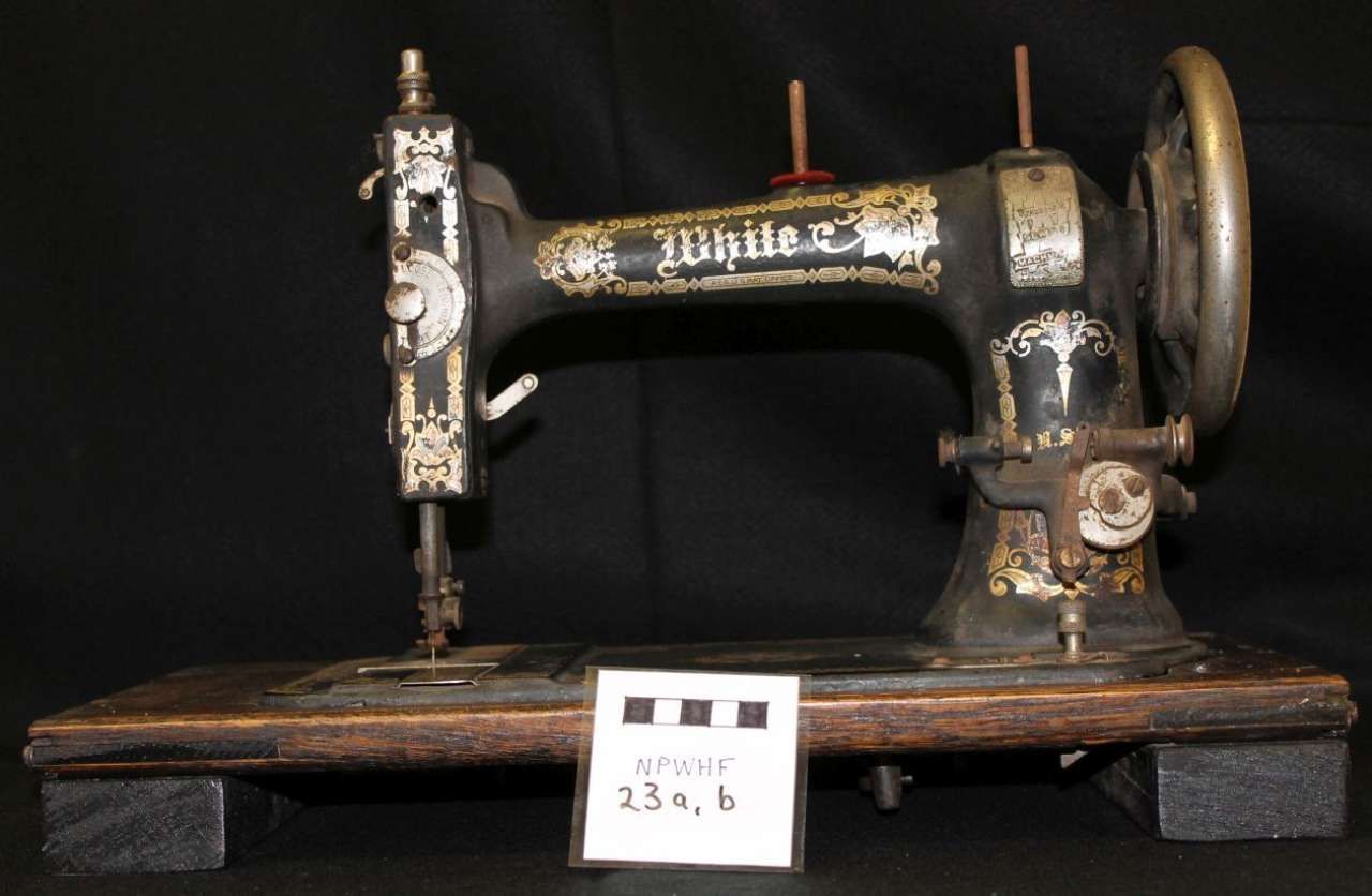 Antique black-and-gold Singer sewing machine on a wooden base against a dark background.