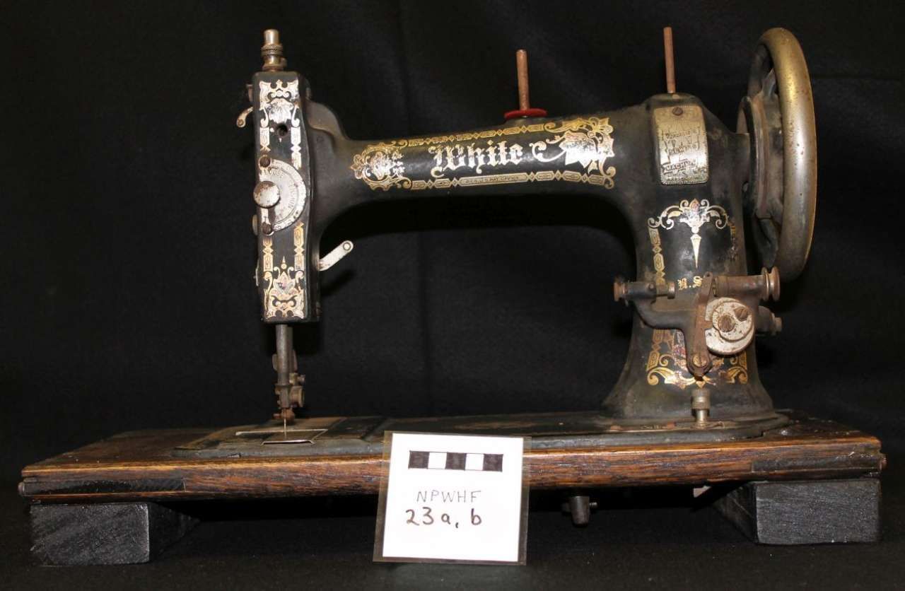 Antique black sewing machine on a wooden base with a small museum label in front