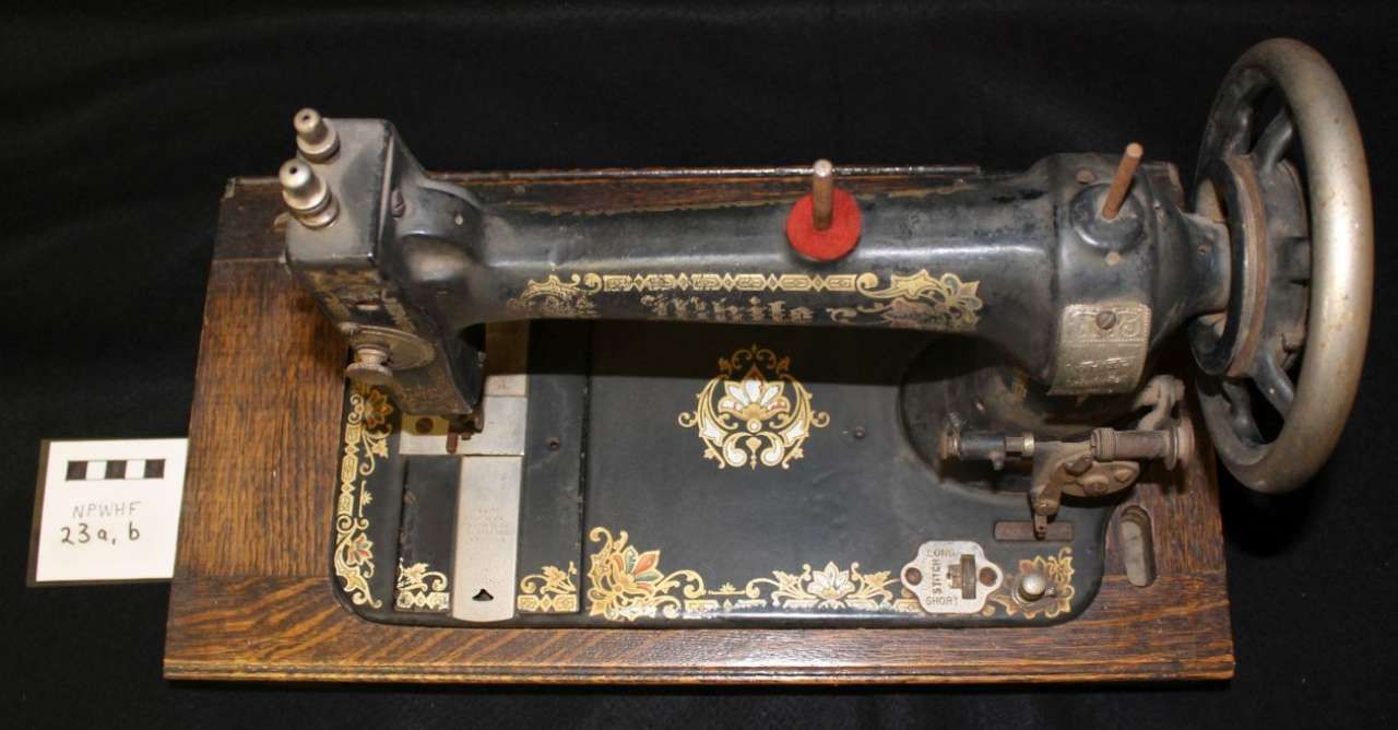 Vintage black sewing machine on a wooden base with a hand wheel and red knob