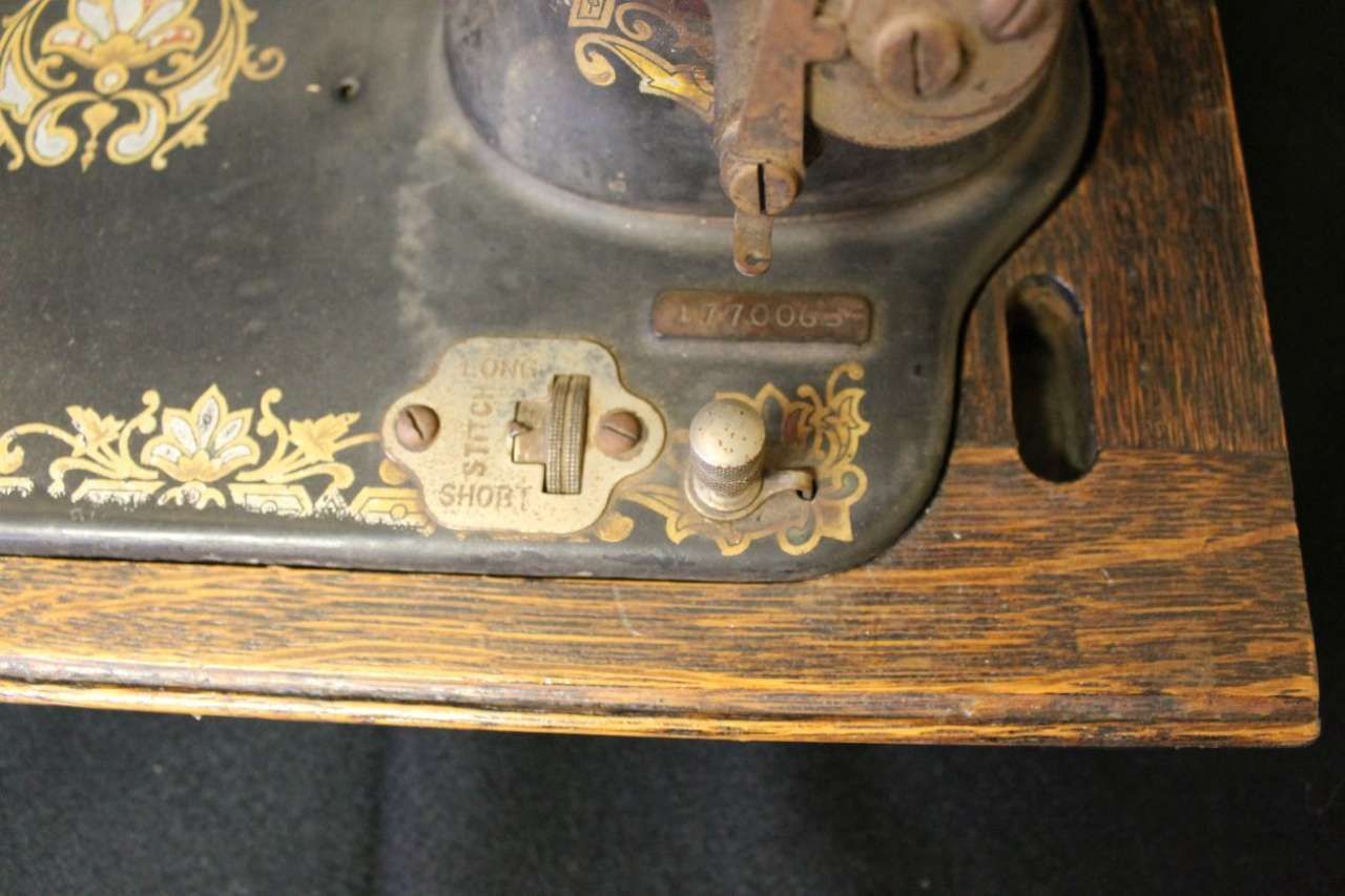 Close-up of an antique wooden sewing machine base with ornate gold floral detailing and metal fittings.