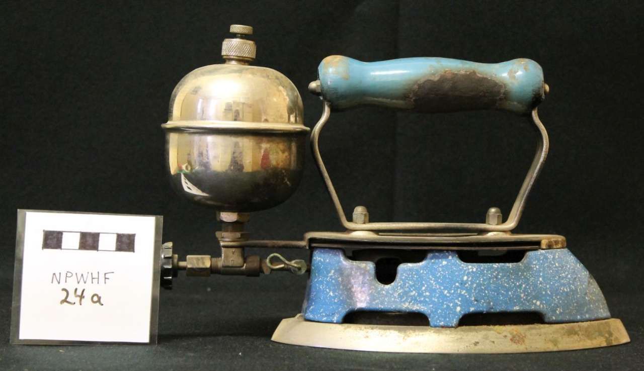 Antique brass-and-blue metal hand pump or toy iron on a black background, with a small label beside it