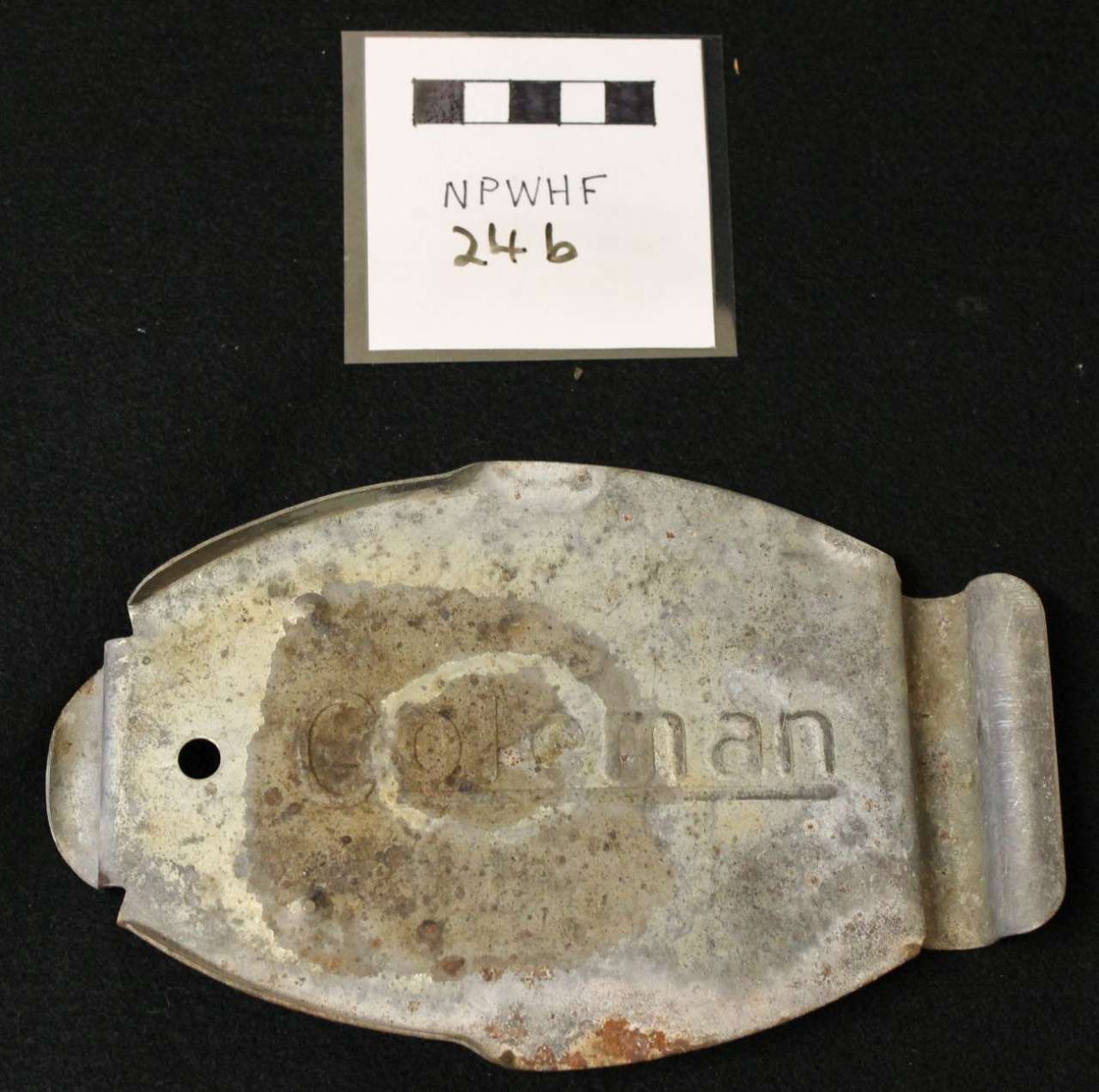 Weathered metal buckle or plate with embossed text, shown beneath a small labeled scale card.