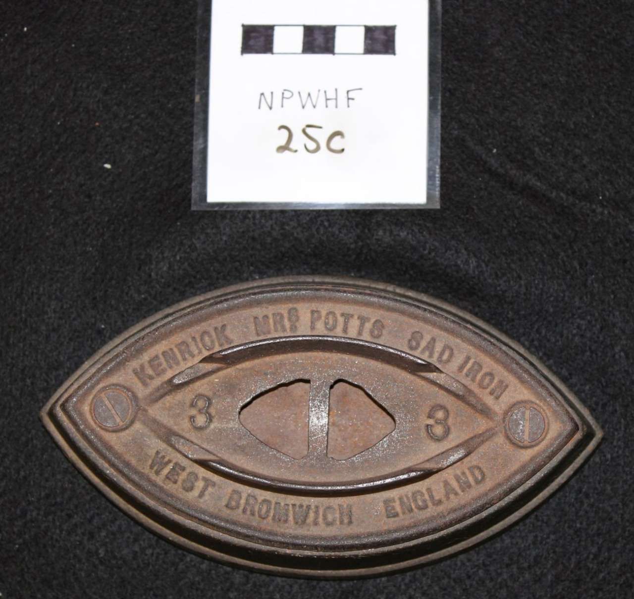 Antique oval metal badge on black background with a small labeled card above it.