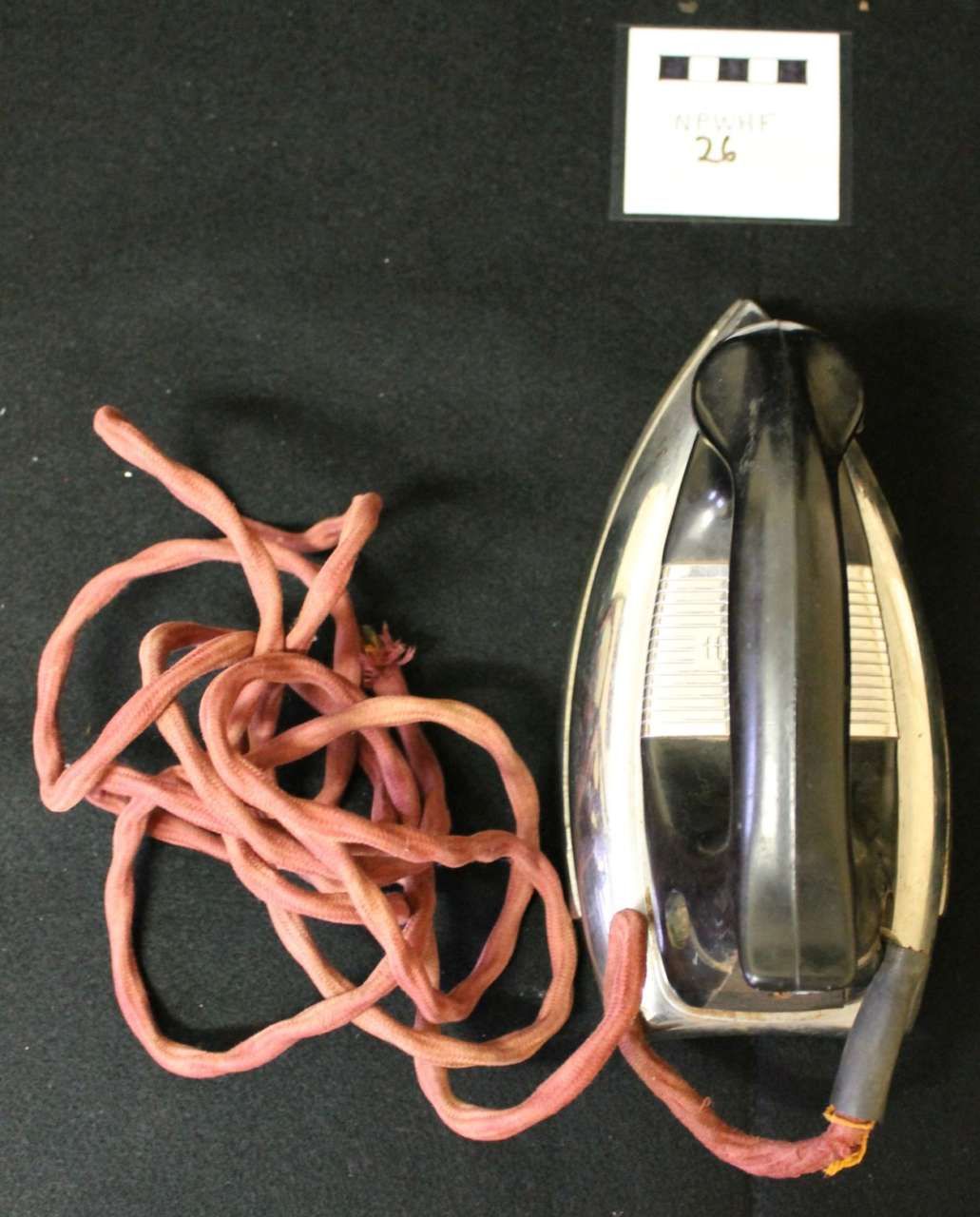 Red cord tangled beside a black and silver iron on a dark background, with a small white adapter above.