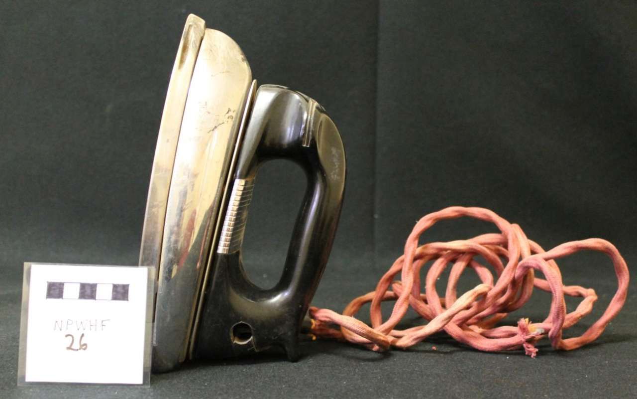 Old electric iron beside a small white box and a tangled pink cord on a dark surface