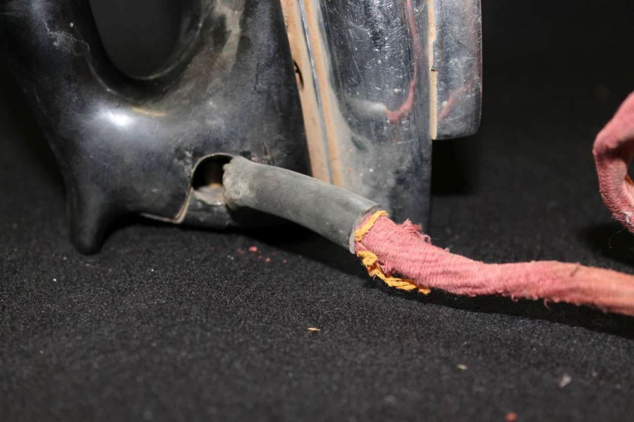 Frayed red electrical wire with exposed yellow inner layer plugged into a dark appliance panel